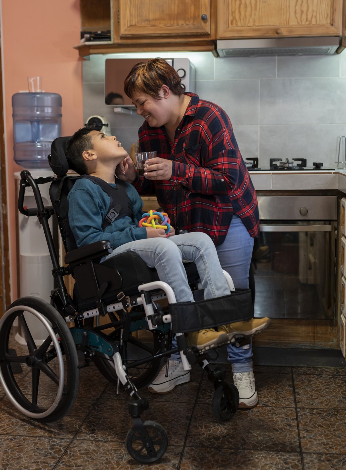 A caregiver offering a drink to a young person who uses a wheelchair